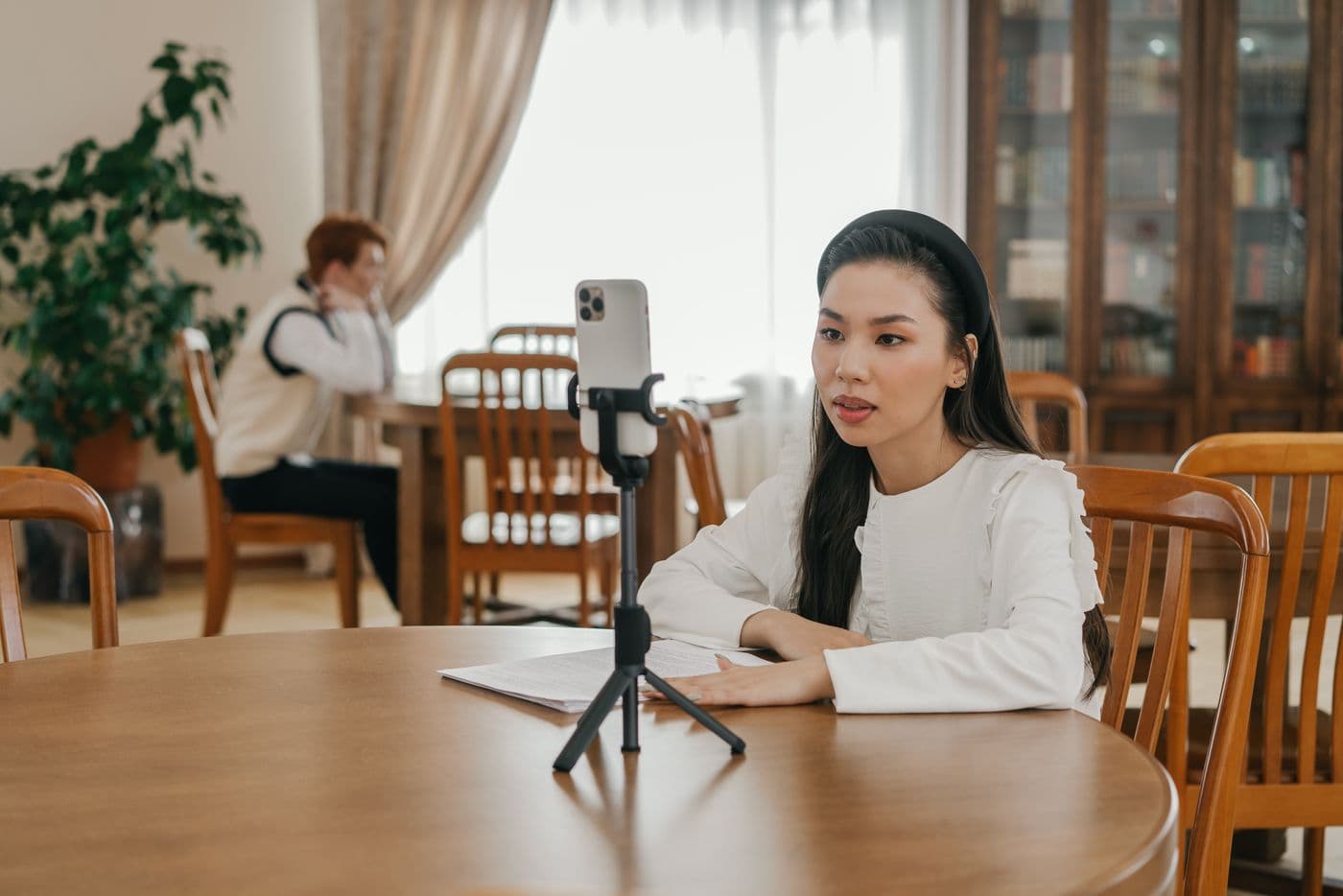 Creator recording a video with a smartphone on a tripod at a wooden table.