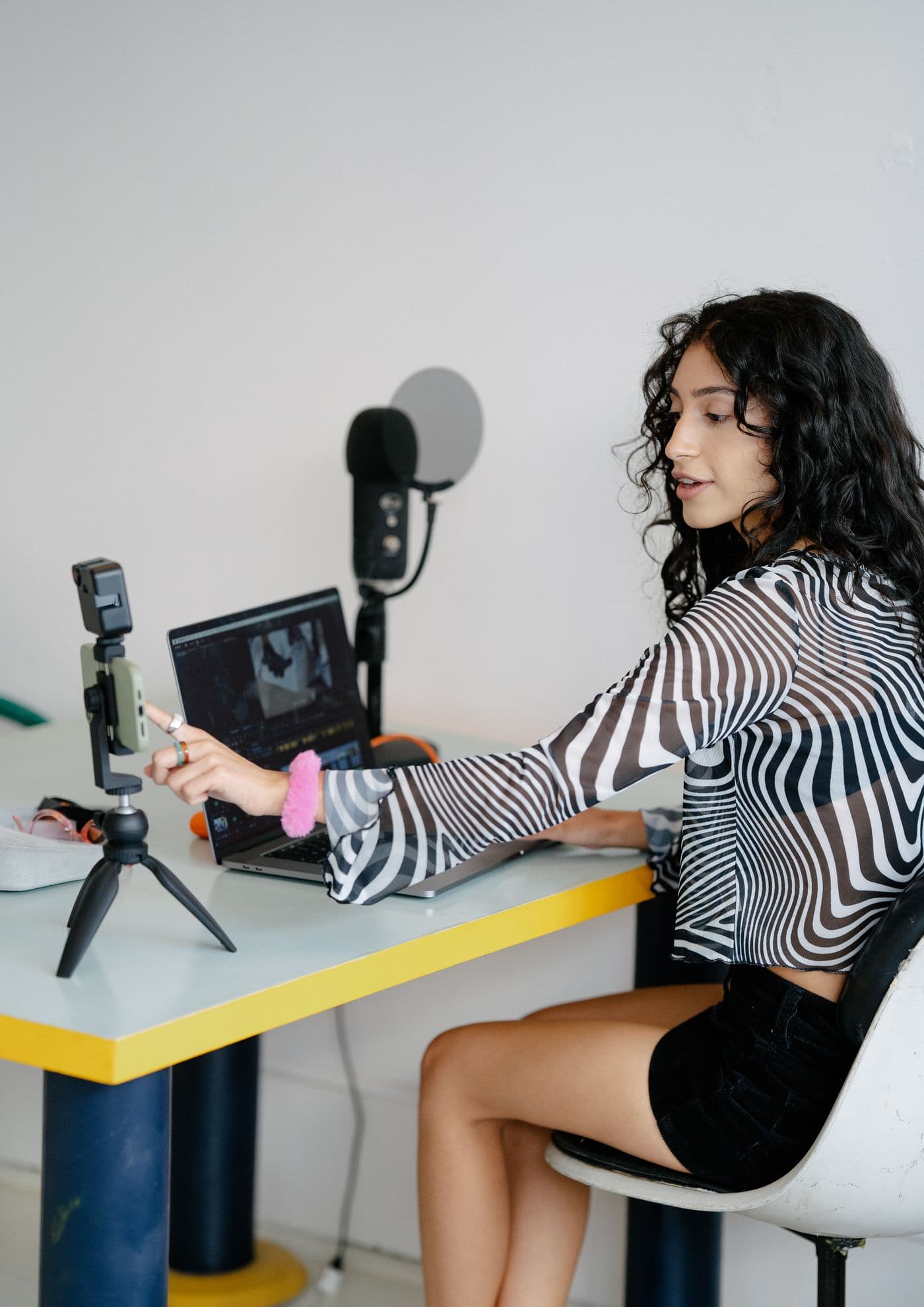 Creator setting up a smartphone beside a laptop and microphone at her desk.